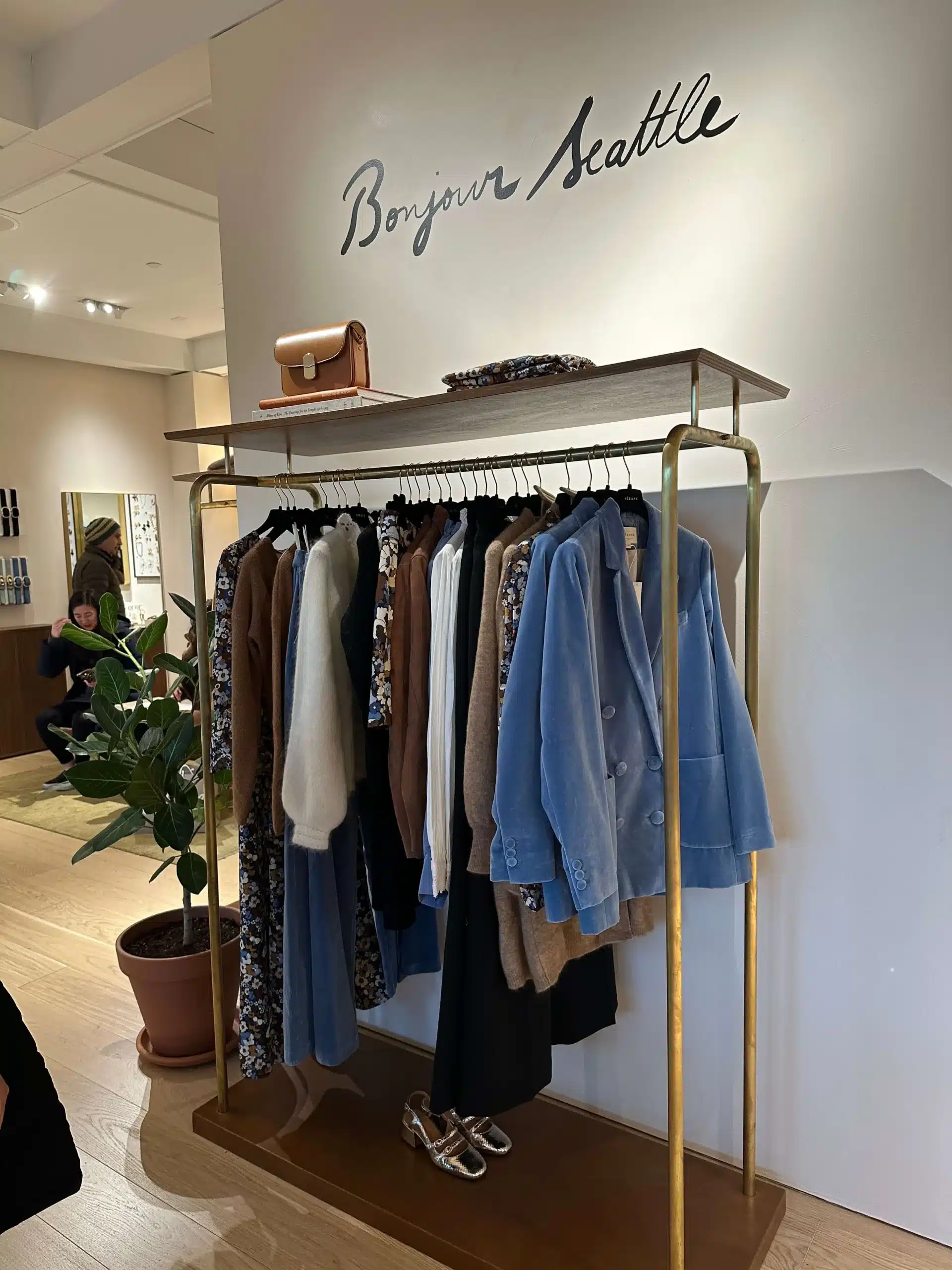 Sezane sweaters, blazers, and dresses hanging on a rack for brands like Sezane
