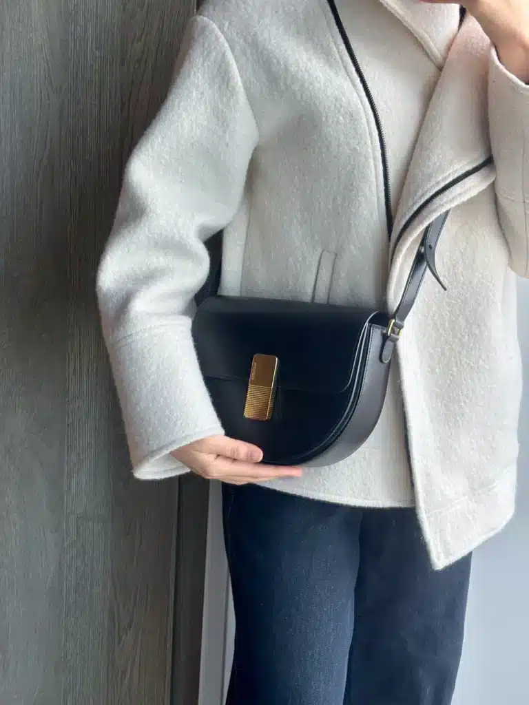 woman wearing Ateliers Auguste bag over white coat and denim pants